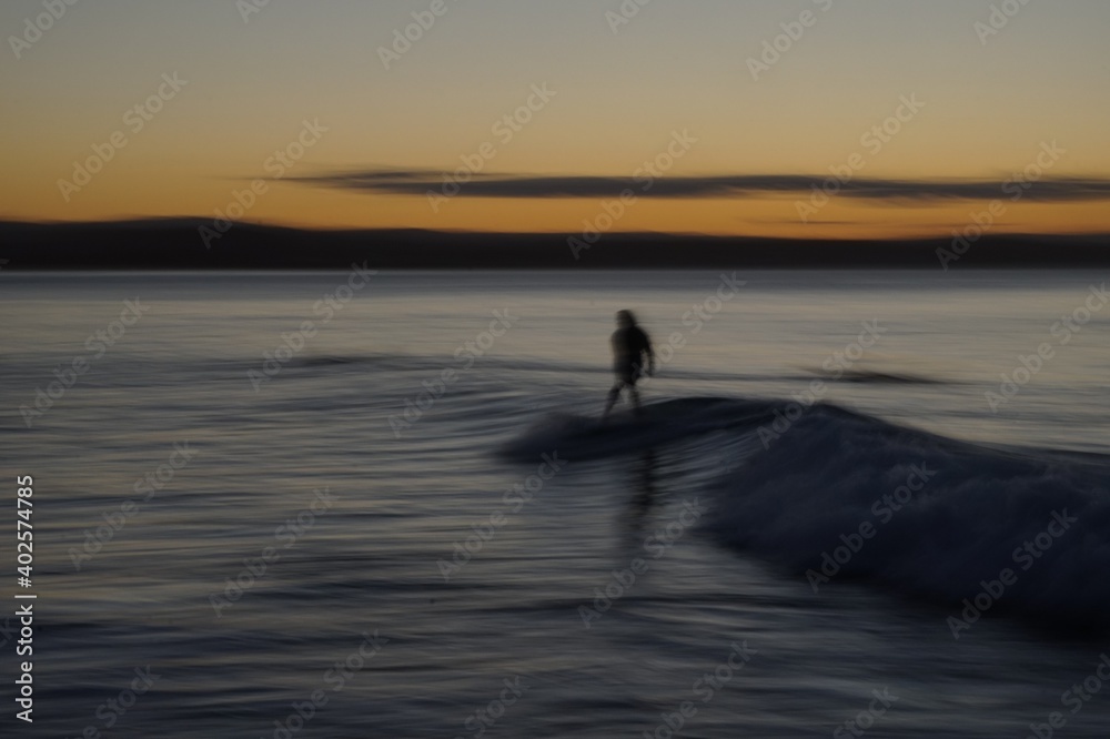 Speed blur - Long exposure of a female surfer riding a colourful wave at sunset on the Gold Coast