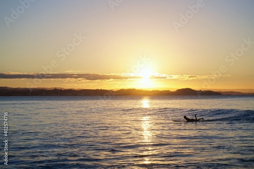 The setting sun reflects off the surface of the ocean as a surfer paddles for a wave - Gold Coast