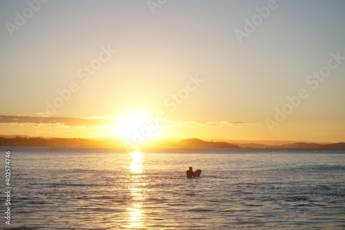 Sunlight reflects off the calm water surface as a surfer sits on his surfboard - Greenmount, Gold Coast