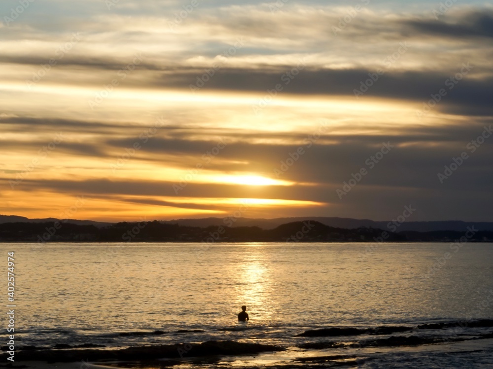 A surfer sat waiting for a wave at sunset at the world famous Snapper Rocks on the Gold Coast - Australia