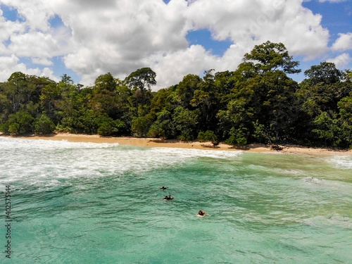 Three surfers paddling out through turquoise waters from the rainforest behind them