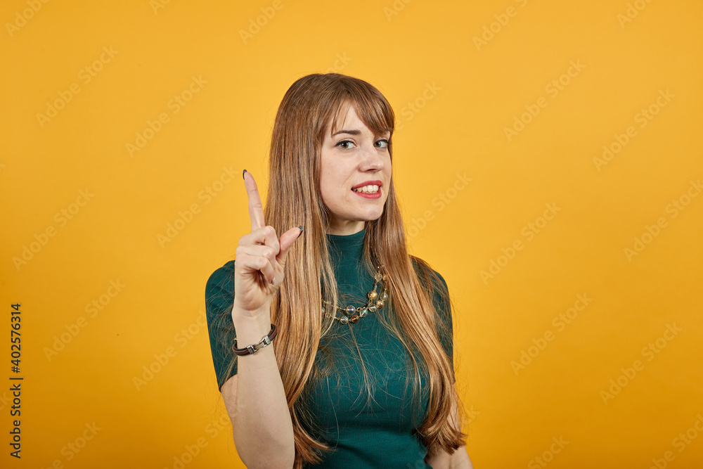 Hand points index finger up, pointing forefinger surprise gift option, great idea. Young attractive woman, dressed green shirt blonde hair, yellow background Hand points index finger up, pointing forefinger surprise gift option, great idea. Young attractive woman, dressed green shirt blonde hair, yellow background