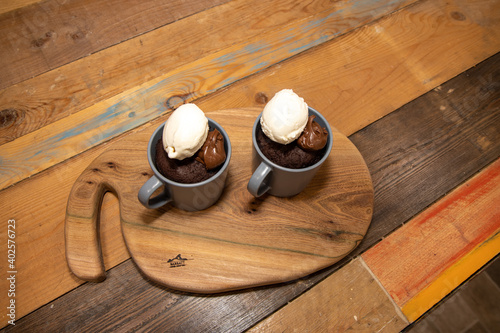 A cup of chocolate cake that has been made in a microwave with chocolate source and ice cream on a wooden kitchen work top photo