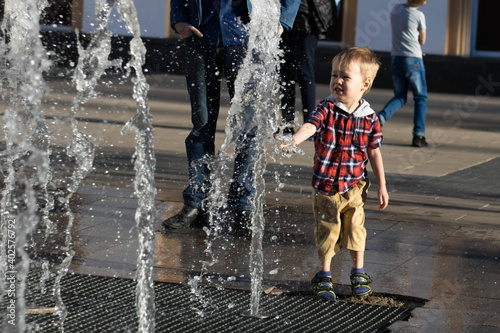 Little boy touches the street fountain and splashes water. Full height
