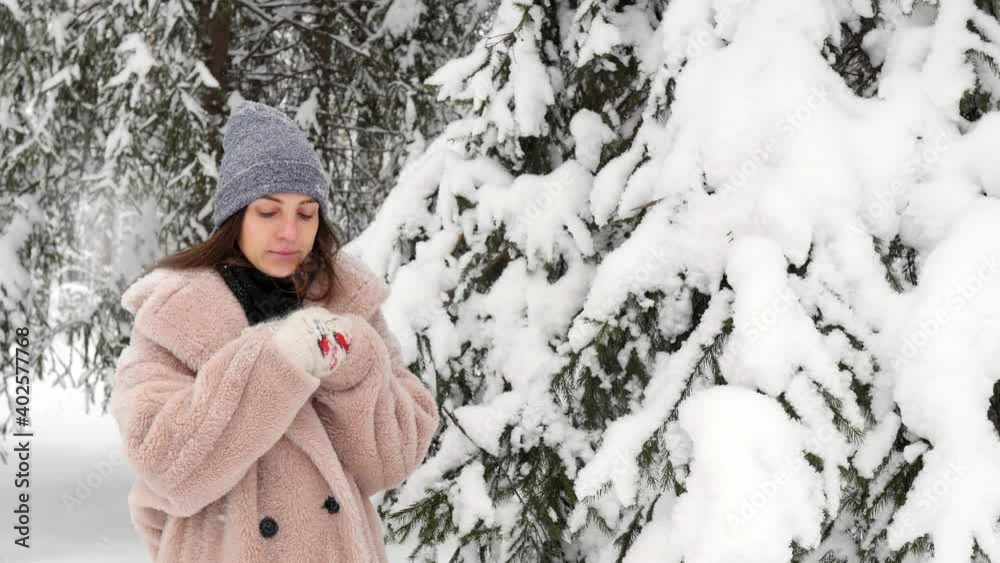 A young woman in a pink fur coat on a winter day warms her hands with steam from her mouth. Winter walks in the woods. Seasonal viral diseases, flu, colds, runny nose. A young woman in a pink fur coat on a winter day warms her hands with steam from her mouth. Winter walks in the woods. Seasonal viral diseases, flu, colds, runny nose.