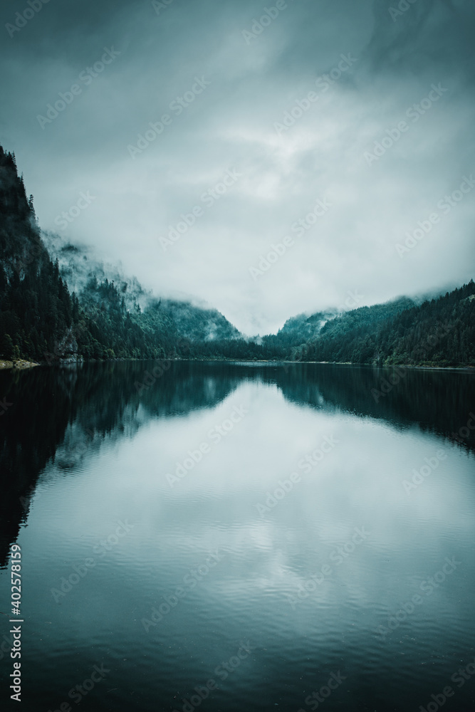 Perfect reflections of mountains in the water of a lake. Moody and foggy weather at a beautiful and peaceful mountain lake. Gosausee, Alps, Austria, Europe