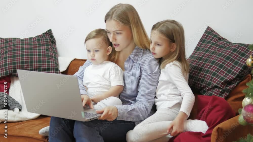 Young mother with little cute children son and daughter sitting on a sofa and using laptop. Family looking at computer, watching film, enjoy using devices together sit on sofa, technology addicted Young mother with little cute children son and daughter sitting on a sofa and using laptop. Family looking at computer, watching film, enjoy using devices together sit on sofa, technology addicted