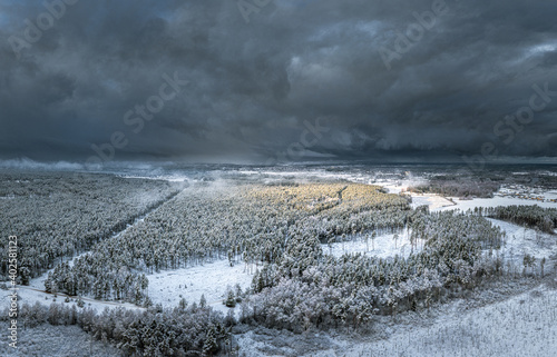 Snowy winter landscape with forest covered in snow. Aerial view over dramatic storm clouds. White scenic countryside.