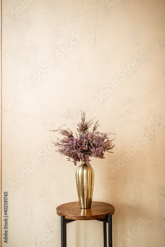 Dried Calluna flower in a gold vase on a beige wall background