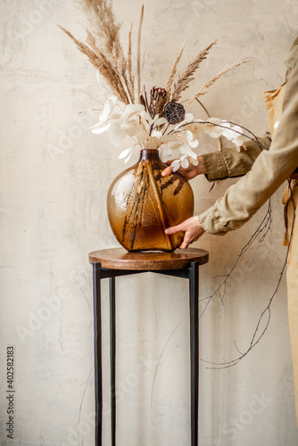 Obraz na plátně Woman decorating home with a composition of dried flowers and herbs in a glass v