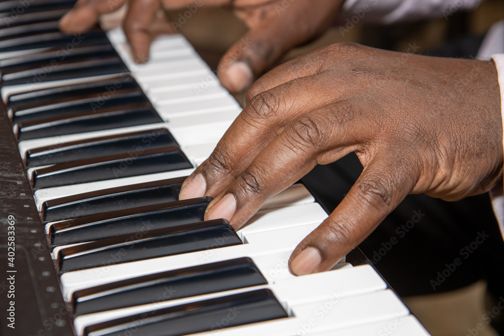 Fototapeta premium Fingers of an old African American man playing a keyboard piano wearing a black suit and pink shirt