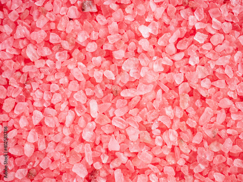 Pink colored salt crystals as a background. Aromatic roseate bath salt with litchi and patchouli scent. Large sprinkled crystals of crimson sea salt. Beauty and body care concept. Close up.