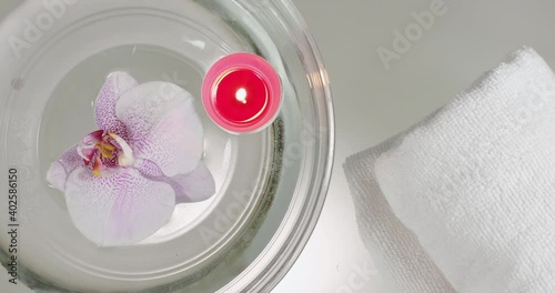 Close-up from above, a white towel is placed on a glass table, next to an archidea floating in the water and a burning candle. Interior details to create the ambience of a spa lounge zone. photo