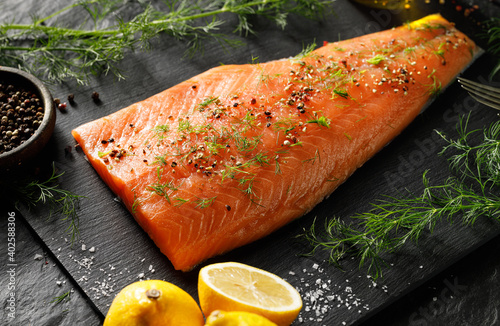 Fresh salmon fillet with spices and fresh herbs on a black background close up view