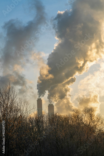 Steam or smoke goes up from pipes of thermal power station in cold weather at sunset or sunrise. Electricity and pollution theme.