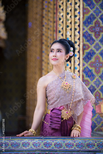 Beautiful Thai woman wearing a Thai Chitralada dress holds a garland in her hand in a Buddhist temple in Thailand which is architecturally beautiful. photo