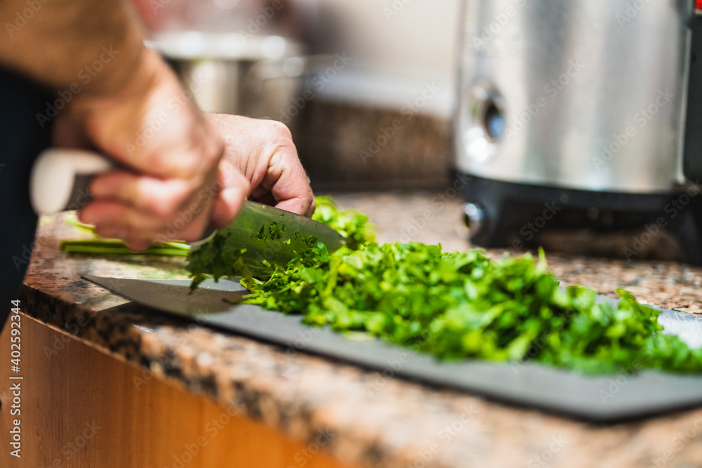 Detail of a man's hands cutting raw parsley with a knife on a cutting board in kitchen. Spain. Mediterranean cuisine