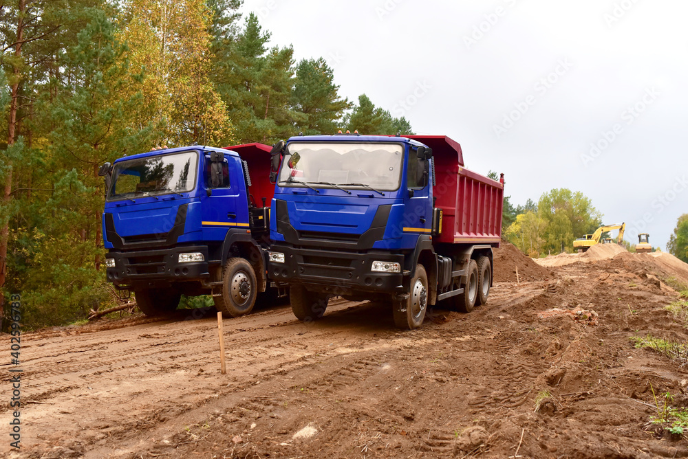 Dump trucks work on road construction in a forest zone. Tipper truck transport sand for roadworks project