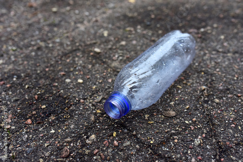 An empty plastic bottle lies on the asphalt. Discarded rubbish on a city street. Environmental pollution concept