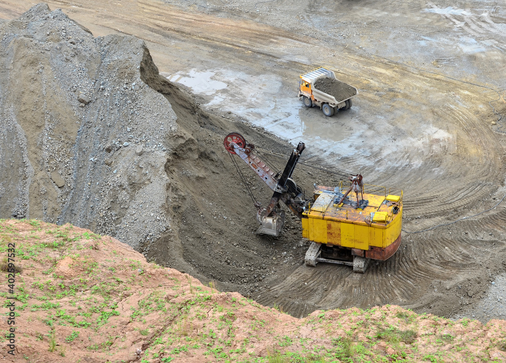 Excavator with electric shovel loading the rocks in mining truck at quarry. Haul truck transports minerals in the open pit. Open-cast mining of extracting rock or minerals from the earth. Excavator with electric shovel loading the rocks in mining truck at quarry. Haul truck transports minerals in the open pit. Open-cast mining of extracting rock or minerals from the earth.