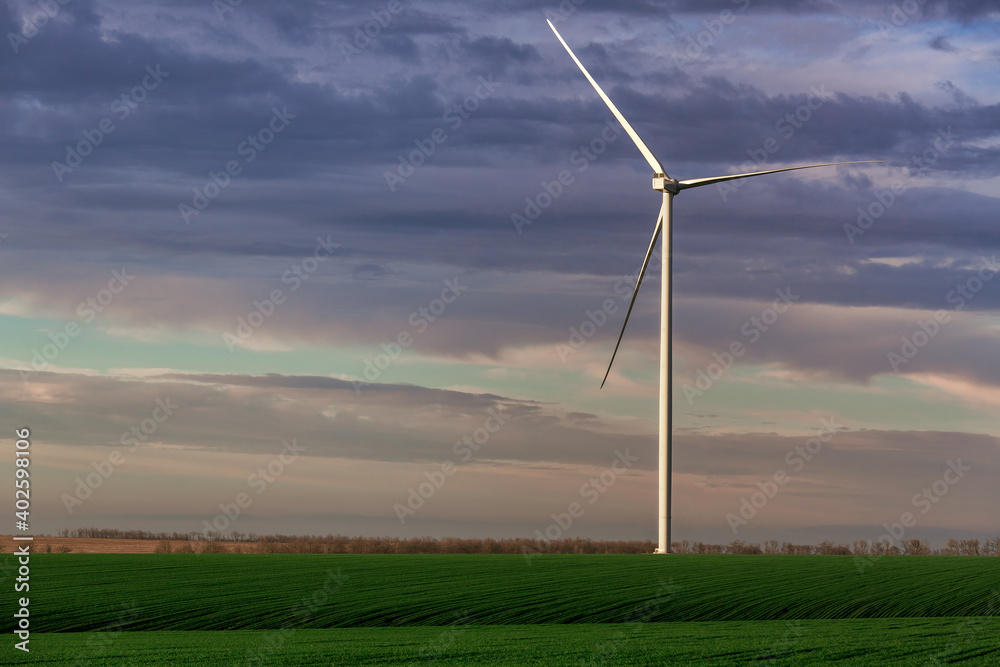 wind power generator in green hilly agricultural fields in the background sky with clouds, zero emissions renewable eco energy production in an outdoor farm. wind power generator in green hilly agricultural fields in the background sky with clouds, zero emissions renewable eco energy production in an outdoor farm.