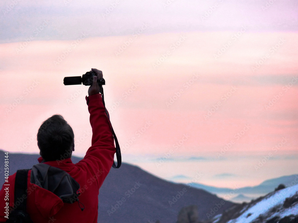 photographer in mountains looking at pink clouds