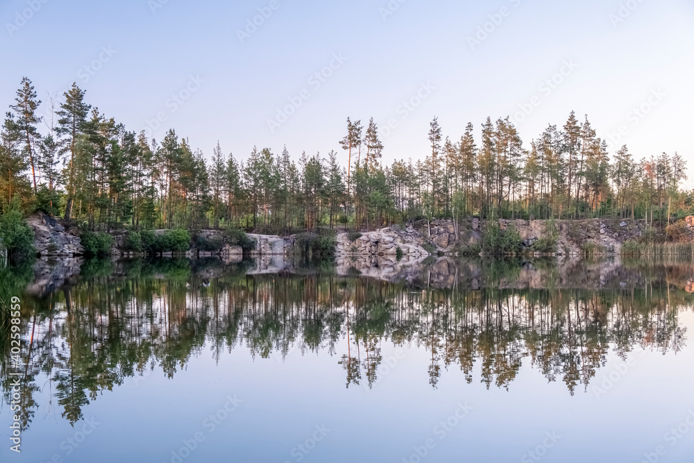 Panoramic view of a beautiful clear lake among granite rocks and a pine forest reflected in the water at sunset in the summer, sun rays shining through the trees, 4k