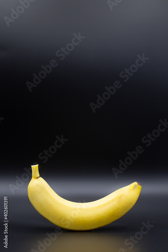 Unpeeled healthy banana free standing against a black background