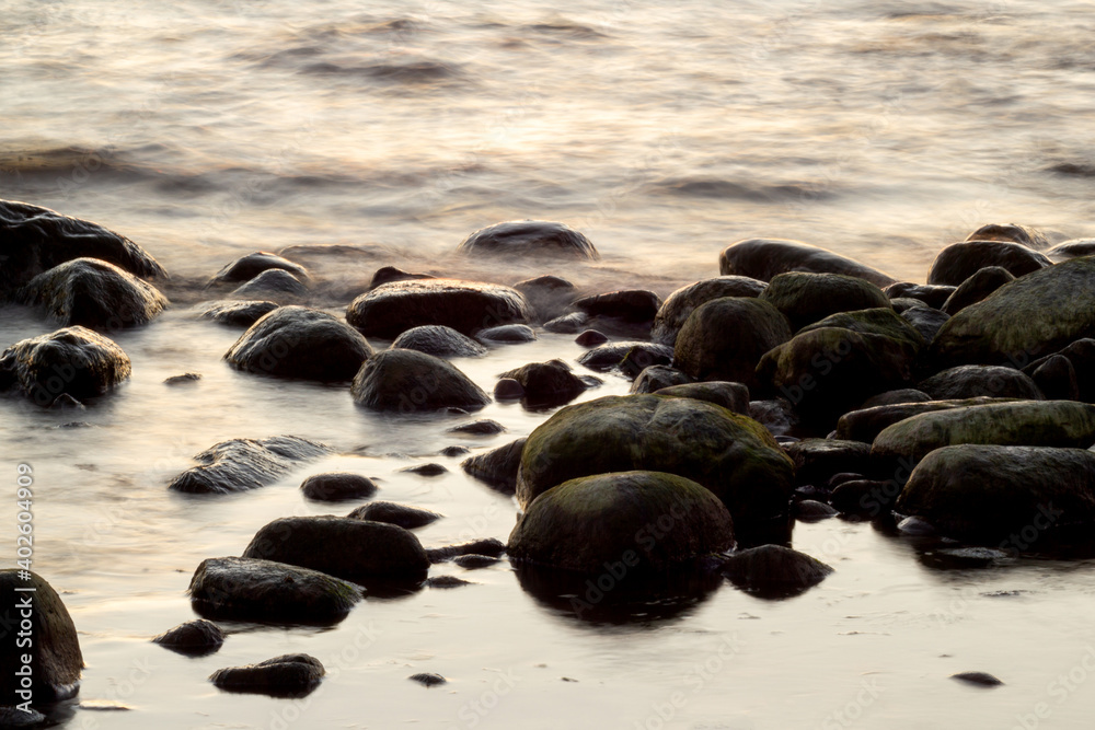 Long exposure of sea and rocks. Boulders sticking out from smooth wavy sea. Tranquil scene. Long exposure of sea and rocks. Boulders sticking out from smooth wavy sea. Tranquil scene.