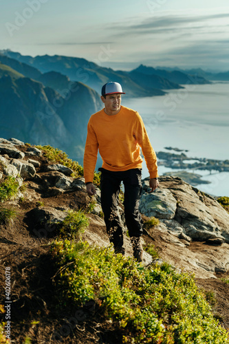 Male in orange top walking on a summit of a mountain after a long hike in Norway, Lofoten