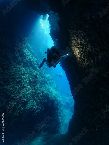 Fototapeta Naklejka Na Ścianę i Meble -  Scuba divers underwater exploring lightcaves blue ocean scenery with torch 
