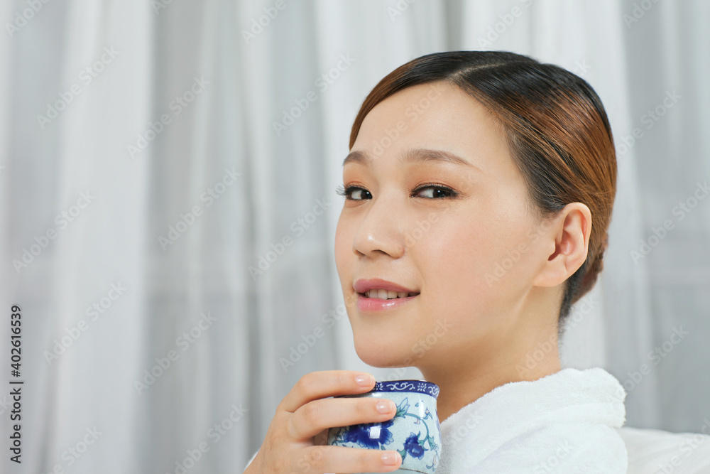 A young woman wearing a bathrobe is drinking tea A young woman wearing a bathrobe is drinking tea
