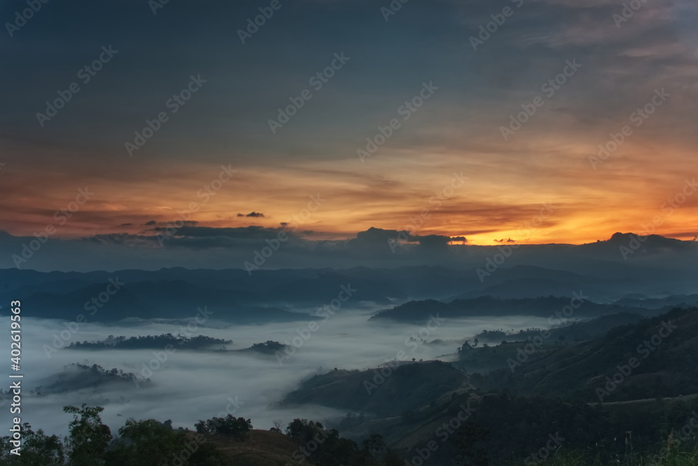 Fluffy fog stream is covering a valley with colorful twilight sky in a morning
