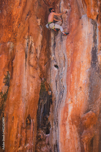 A strong man climbs a beautiful orange rock.