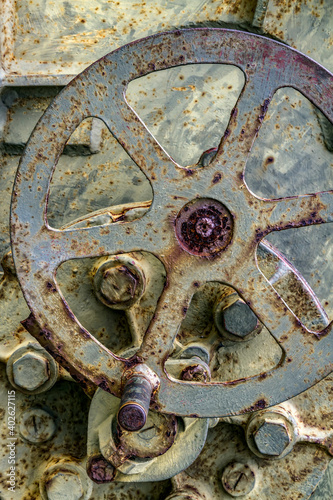 A metal control wheel on an old, decrepit piece of machinery is showing some rust and age.