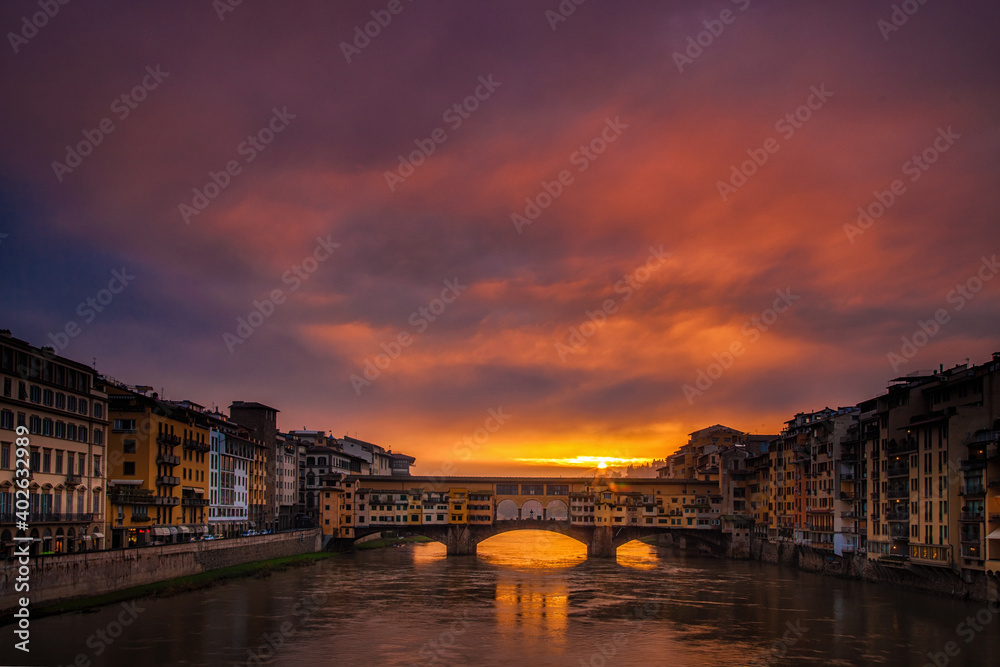 Sun peeking through clouds at dawn over the Ponte Vecchio in Florence, Italy