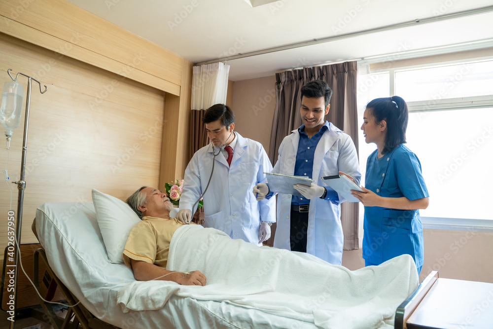 Medical Team On rounds meeting around bed of senior male patient at hospital,Doctors discussing the report on clipboard. Medical Team On rounds meeting around bed of senior male patient at hospital,Doctors discussing the report on clipboard.