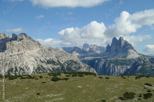 A distant view on Drei Zinnen from Strudelkopf in Italian Dolomites. The famous mountains are surrounded by many massive mountain chains. A lush green meadow in front. High Alpine landscape. Freedom photo