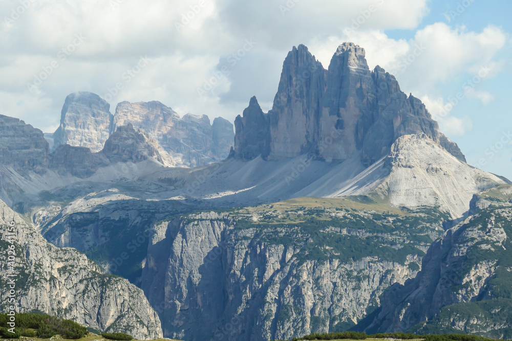 A distant view on Drei Zinnen from Strudelkopf in Italian Dolomites. The famous mountains are surrounded by many massive mountain chains. A lush green meadow in front. High Alpine landscape. Freedom