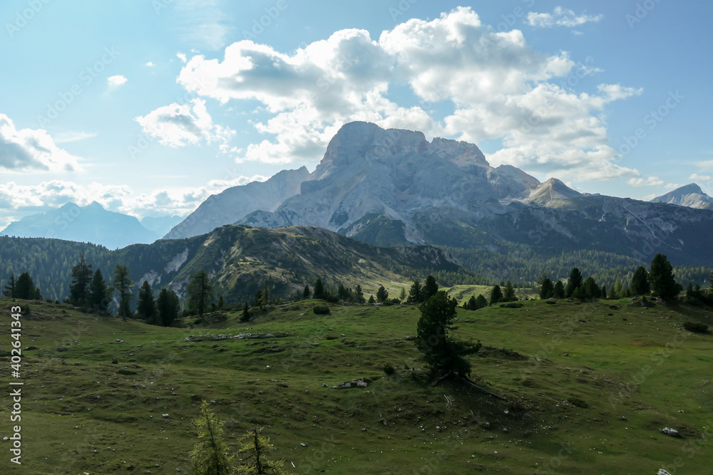 A panoramic view on the high Italian Dolomites from the top of Strudelkopf. There is a wide gravelled path leading to the top. Sunny day. A few clouds above the high peaks. Lush green plateau around