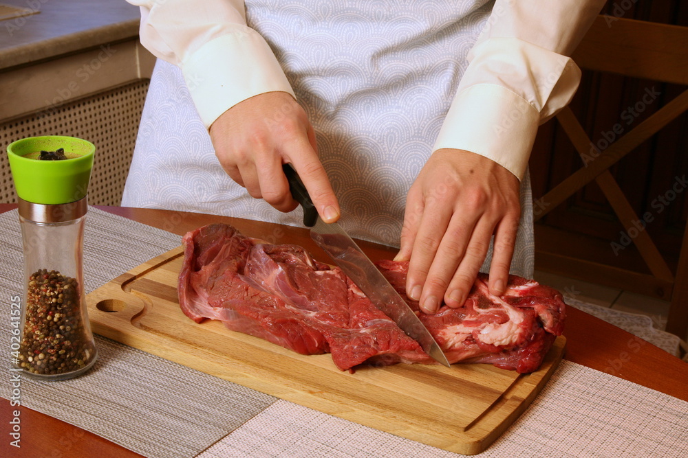 Male hands are cutting raw meat