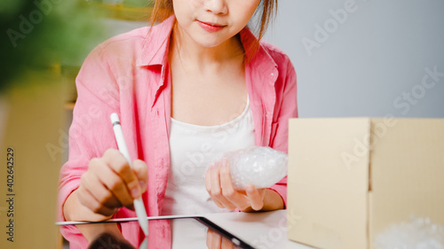 Young Asia entrepreneur businesswoman check product purchase order on stock and save to tablet computer work at home office. Small business owner  online market delivery  lifestyle freelance concept.