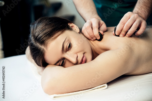 A beautiful girl lies on her stomach during a stone massage. Hands of a massage therapist massaging the shoulder.