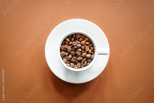 Top view of roasted coffee beans in white coffee cup with brown background 
