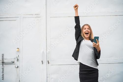 Outdoor portrait of ecstatic modern businesswoman who is joyful. She is holding smartphone.