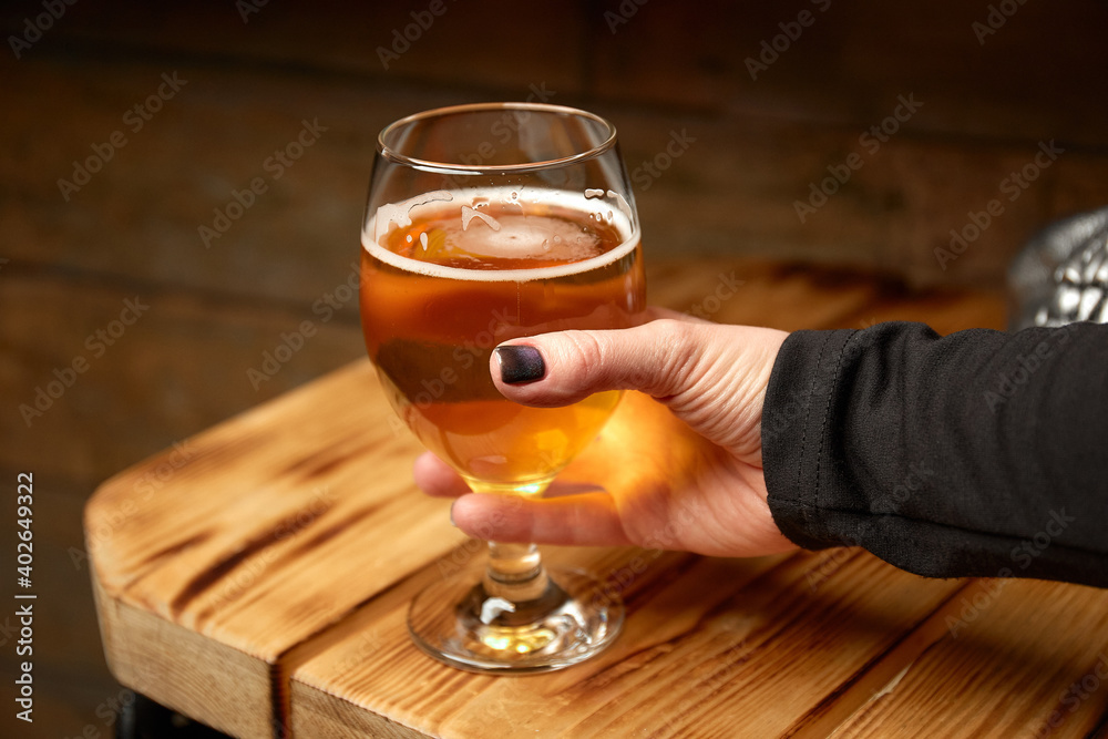 The girl holds in her hand a glass of beer, next to it lies a mask-skull. Close-up. Against the background of a wooden table. The girl holds in her hand a glass of beer, next to it lies a mask-skull. Close-up. Against the background of a wooden table.