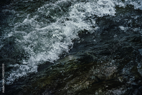 Nature background of dark water stream of mountain river with rapids. Full frame of sea surf. Natural textured backdrop of ocean surf. Texture of tide close-up. Dark water surface of mountain creek.
