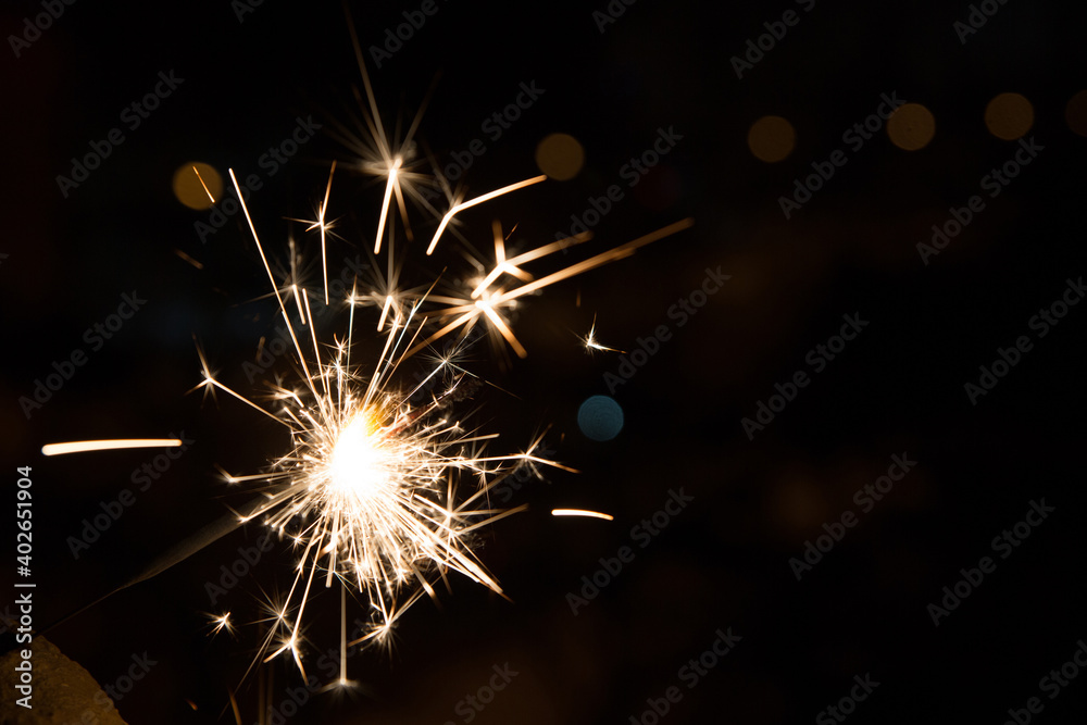 Obraz premium Bengal fire sparkles against the background of city lights, blurred bokeh. A lot of sparks