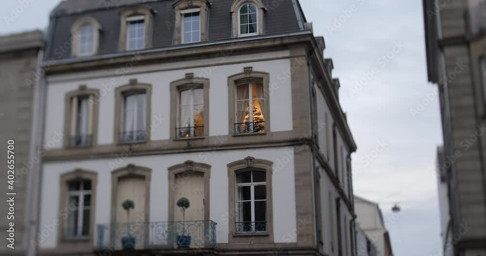 Slow tilt-shift focus on the luxury Haussmannian villa apartment building with only on the window being lit and Christmas tree inside - low angle view from street Slow tilt-shift focus on the luxury Haussmannian villa apartment building with only on the window being lit and Christmas tree inside - low angle view from street
