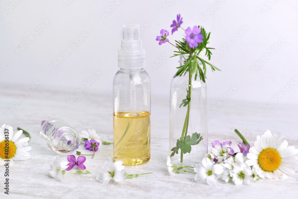 bottle of  essential oil and fresh wild   flowers  on  a table on white table